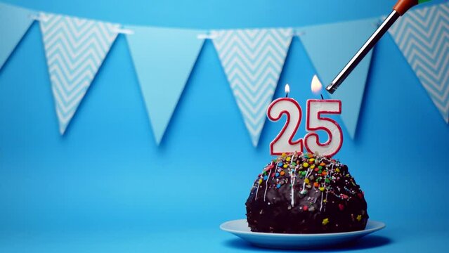 chocolate birthday cake with a burning candle number twenty five, 25 on a blue background. Copy space. place for text
