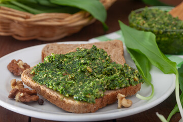 Wild leek pesto with olive oil and wallnuts on a wooden table. Spread and leaves of fresh ramson. Healthy vegan spread for breakfast.