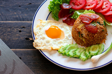 Fried rice with chinese sausage served in a white plate with fried egg, tomato and lettuce.