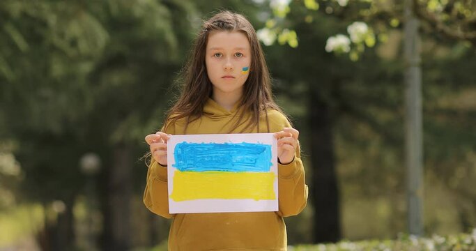 Serious face of a little girl. The child's cheeks are painted with the yellow and blue colors of the Ukrainian flag. Children ask for peace.