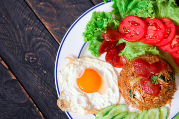 Fried rice with chinese sausage served in a white plate with fried egg, tomato and lettuce.