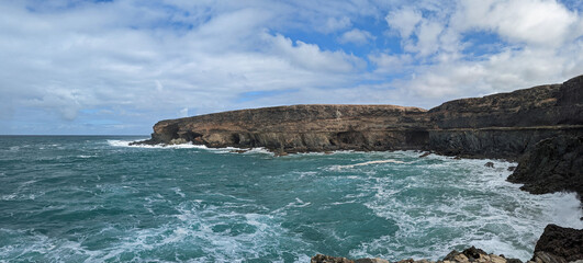 Rocky cliffs at Ajuy on the island of Fuerteventura part of the Canary Islands with a choppy turquoise sea and a cloudy sky