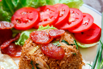 Fried rice with chinese sausage served in a white plate with fried egg, tomato and lettuce.