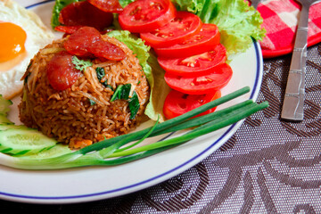 Fried rice with chinese sausage served in a white plate with fried egg, tomato and lettuce.