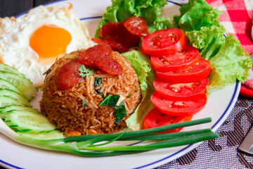 Fried rice with chinese sausage served in a white plate with fried egg, tomato and lettuce.