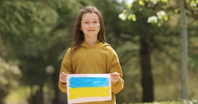 smiling Ukrainian child girl with flag of Ukraine outdoors. No War outdoors. Crisis, peace, stop aggression, child against Russian war