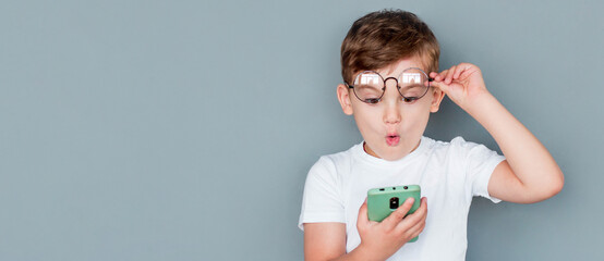 Shocked child boy using smartphone and taking off glasses on gray background