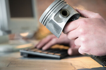 Car service worker with a engine piston in hand orders a car spare parts through the internet with the computer concept.