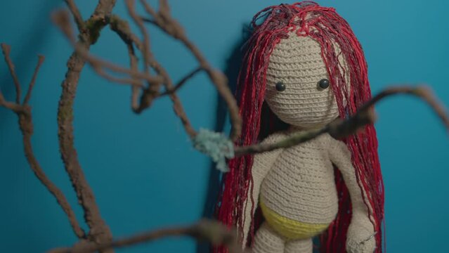 Knitted doll with dreadlocks hanging on wall. Handmade soft toy with hairstyle on blue wall. Concept of interior and beauty.