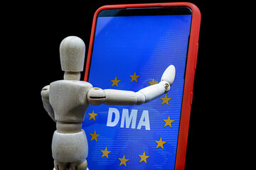 wooden mannequin touching a smartphone with the text DMA and the flag of the european union on the...
