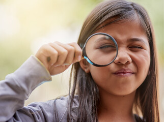 Shes on another one of her explorations. Portrait of a little girl looking through a magnifying glass.