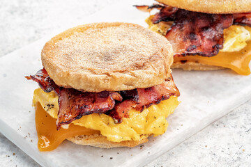 English muffin, scrumbled egg, ham, and cheese breakfast sandwich on a cutting board