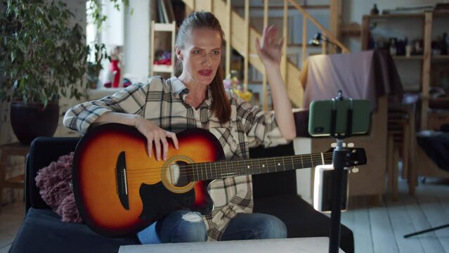 A woman writes a video blog on her phone and talks about how to play the guitar