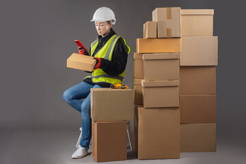 Warehouse worker. Girl is heading phone to box. Concept preparing parcel for shipment to buyer. Cardboard parcels on black. Warehouse terminal near warehouse manager. Career in fulfillment business