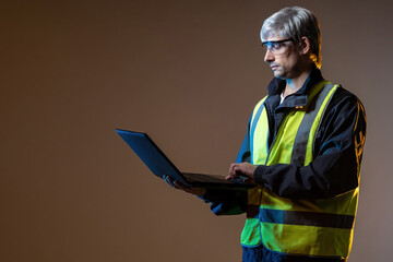 Builder designer. Designer with laptop in hand. Builder on brown background. Gray-haired man with open laptop. Man who works as designer for construction company. Engineer and computer
