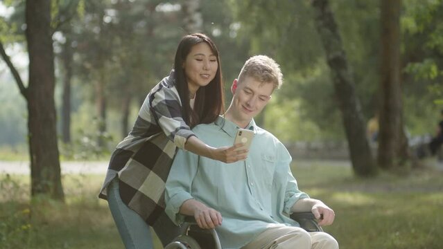 A pretty couple is making selfies together, smiling and posing in the public park in a good weather