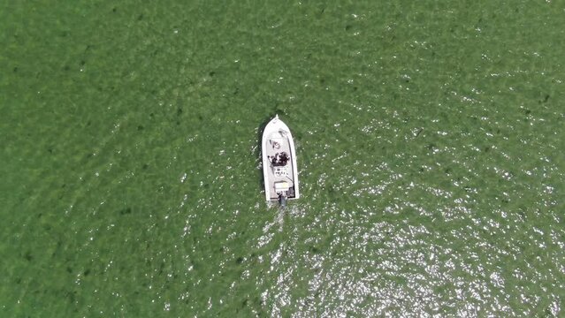 Top down aerial of small fishing boat in emerald green water static drone shot