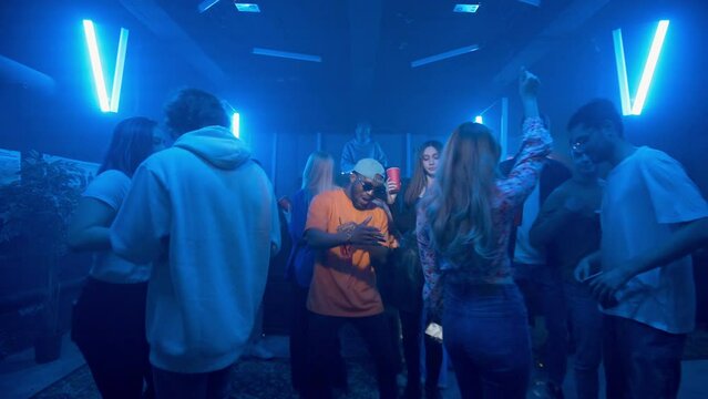 An African-American man dances in a crowd in a nightclub on the dance floor under the light of colored spotlights. Night club