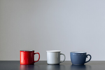 Three cups of different colors on a blue table on a gray background