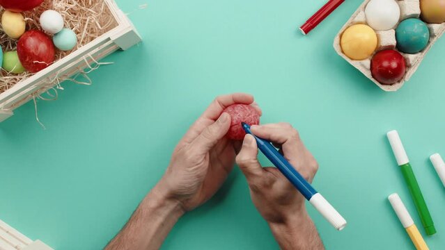 Hand of a man is painting colored Easter eggs