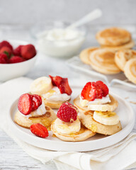 Golden delicious pancakes, honey, summer fruits on white wooden background with space for text. Romantic breakfast and traditional food for Shrove Tuesday. American cuisine, selective focus.
