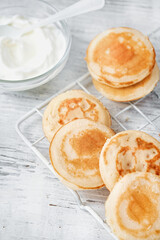 Trendy Golden mini  pancakes, yogurt on white wooden background with space for text, selective focus. Romantic breakfast and traditional food for Shrove Tuesday. American cuisine, selective focus.