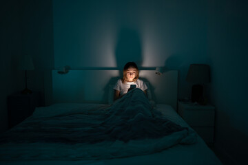 Fototapeta Sleepy exhausted woman lying in bed using smartphone, can not sleep. Insomnia, addiction concept. Sad girl bored in bed scrolling through social networks on mobile phone late at night in dark bedroom. obraz
