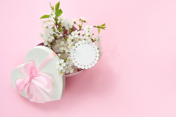 heart gift box with white cherry flowers and empty paper card on abstract pink background. spring season, festive composition. romantic gift for women. top view. copy space