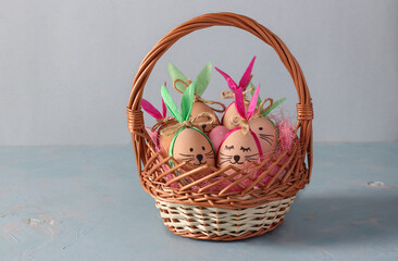 Easter bunnies made of eggs with multi-colored ears made of colored paper lokated in basket on blue...