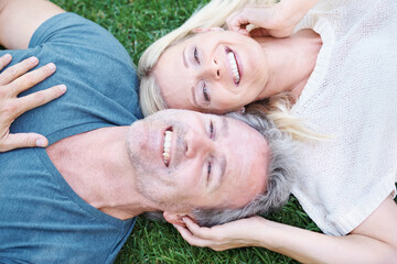 Blissful relaxation brings the happiness. A mature couple lying on the grass and looking up at you happily.