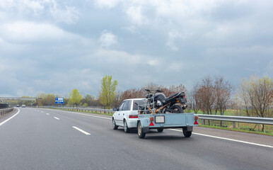 Fototapeta na wymiar White car driving on highway with trailer holding motorcycle