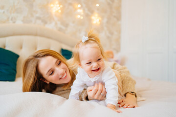 Cute mom and baby daughter lie down, play and hug in bed. games with children. 