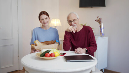An elderly man and a young girl sit at a table in a large bright room and look at each other
