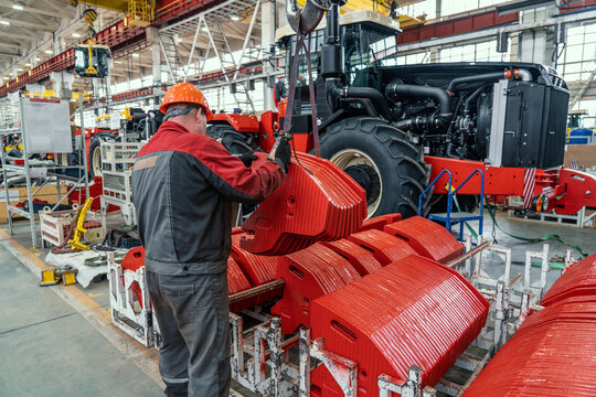 Industrial worker assembles agricultural equipment in tractor or combine harvester production line in factory.