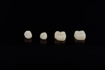 Qualified anatomic ceramic and zirconia crowns of human teeth close up macro isolated on black background.