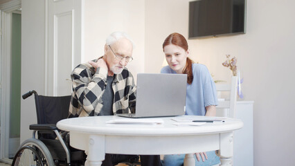 Woman helping disabled grandfather understand how to use laptop