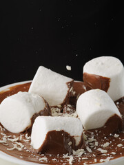 Macro shot. White marshmallow cubes in chocolate paste. Isolated on black background. There are no people in the photo. Sweets, dessert, kids food, calorie breakfast, birthday, holiday.