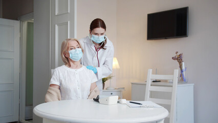 The doctor examines the patient. She is using a stethoscope to listen to the lungs of an elderly...