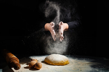women kneads dough and scatters flour on a black background.