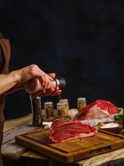 Steaks from raw beef, pork, veal from the farm, cooked by the hands of a professional chef on a wooden cutting board, dark blue background. The concept is recipes for restaurant and home cooking.