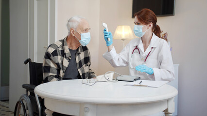 A doctor measures the temperature of an elderly disabled person using an electronic thermometer