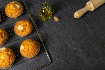 homemade muffins on a baking tray, freshly baked, olive oil, black slate background, space for text.