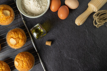 freshly baked homemade muffins on a baking tray, olive oil, fresh eggs, wholemeal flour, black slate background, space for text.