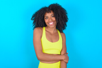 young woman with afro hairstyle in sportswear against blue background laughing.