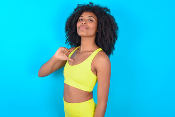 Closeup of cheerful young woman with afro hairstyle in sportswear against blue background looks...