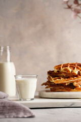 Sweet breakfast - fresh homemade belgian waffles with honey and powdered sugar stacked on white round marble board and small glass with milk