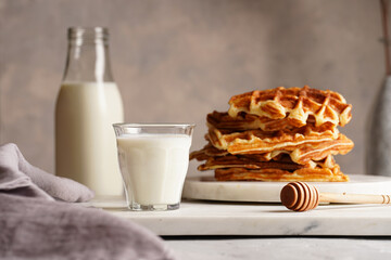 Sweet breakfast - fresh homemade belgian waffles with honey and powdered sugar stacked on white round marble board and small glass with milk
