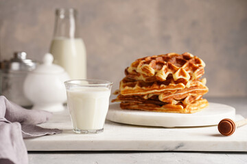 Sweet breakfast - fresh homemade belgian waffles with honey and powdered sugar stacked on white round marble board and small glass with milk