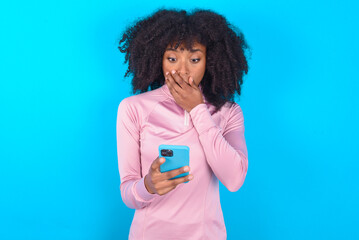 young woman with afro hairstyle in technical sports shirt against blue background being deeply...