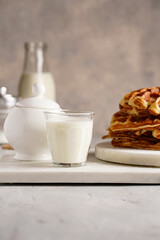 Sweet breakfast - fresh homemade belgian waffles with honey and powdered sugar stacked on white round marble board and small glass with milk